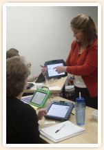 A woman demonstrating communication devices to people seated at a table